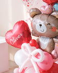 Close up image of a Valentine's Day balloon present featuring a heart-shaped balloon with the name 'Olivia', a teddy bear holding balloons