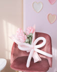 A bouquet of pink balloon roses with a pink balloon bow on a pink chair against a pink wall with heart decorations.