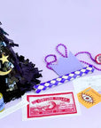 Decorative items including a black hat with stars, beads, and a fortune teller card on a light purple background.