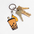 A metal keychain featuring a corgi dog in a bubble tea shop setting, with the keychain attached to a set of keys.