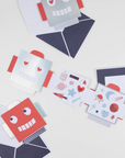 A set of robot-themed Valentine's Day cards and stickers with one card open to show a red interior and a smiling robot face, placed next to its matching envelope.