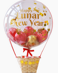 A clear hot air balloon with a Lunar New Year theme, featuring red and gold colors, with a basket containing fake fruit and a 'Happy Lunar New Year' message.