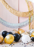 Assorted gold, silver, black, and white balloons scattered on the floor around a pink wall, with some balloons uninflated and others inflated.