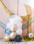 Assorted gold, silver, black, and white balloons in a plastic bag