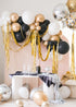 Assorted gold, silver, black, and white balloons scattered on the floor around a pink wall