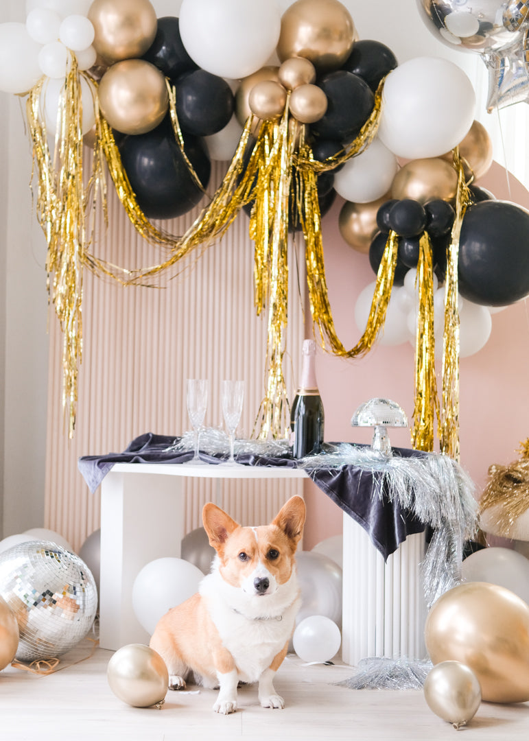 Assorted gold, silver, black, and white balloons scattered on the floor around a pink wall