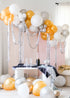 A balloon garland made of silver and gold balloons, set up in a room with a pink wall and a table with a bottle.