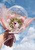 A clear balloon with 'Congratulations' text, filled with pink faux flowers, tied with a ribbon against a blue sky background.