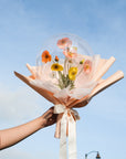 A balloon bouquet arrangement with spring poppies faux flowers, wrapped in peach and white materials against a blue sky.